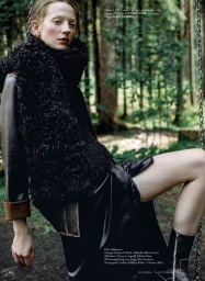 Model wearing a black furry vest sitting on a swing in a dense forest setting