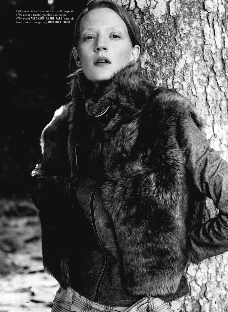 Model leaning against a large tree trunk wearing a dark fur vest and collared shirt in a monochrome outdoor editorial.