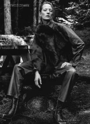 Model seated outdoors in a forest wearing dark leather attire with a fur stole for iO Donna Wild editorial