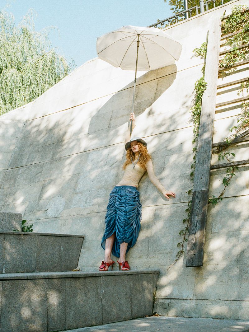 Model with red hair holding white umbrella against stone wall for Cake Magazine editorial