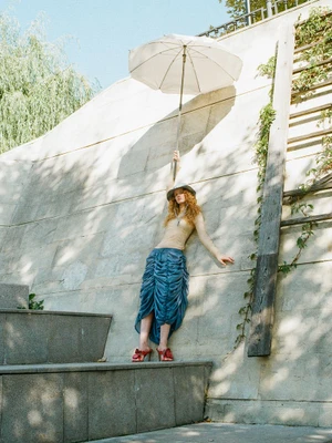 Model with red hair holding white umbrella against stone wall for Cake Magazine editorial