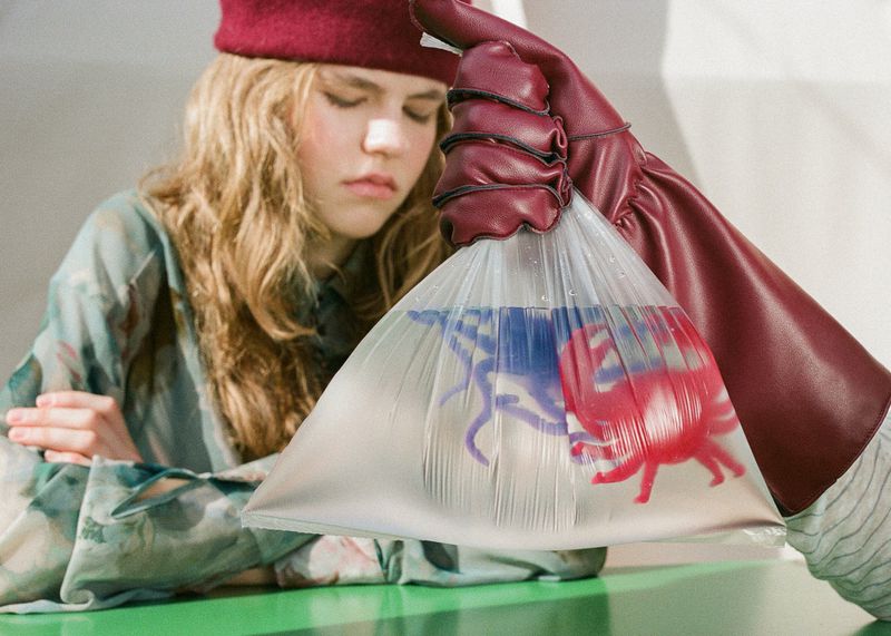 Model wearing a red beret holding a plastic bag containing water and toy sea creatures