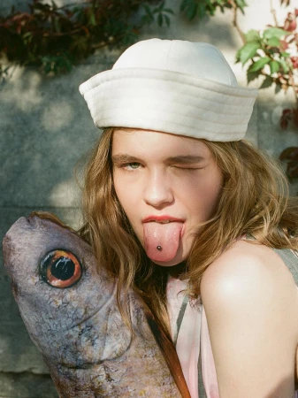 Close-up of a model wearing a white sailor cap holding a large fish prop for Cake Magazine The Last Catch editorial.