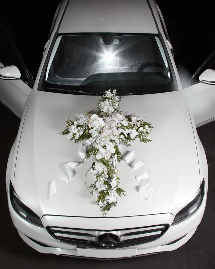High-angle view of a white luxury car with a large floral arrangement and white ribbon on the hood.