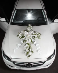 High-angle view of a white luxury car with a large floral arrangement and white ribbon on the hood.