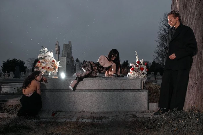 Three figures pose in a cemetery at dusk with floral arrangements on a stone tomb, captured in a moody editorial by Geray Mena.