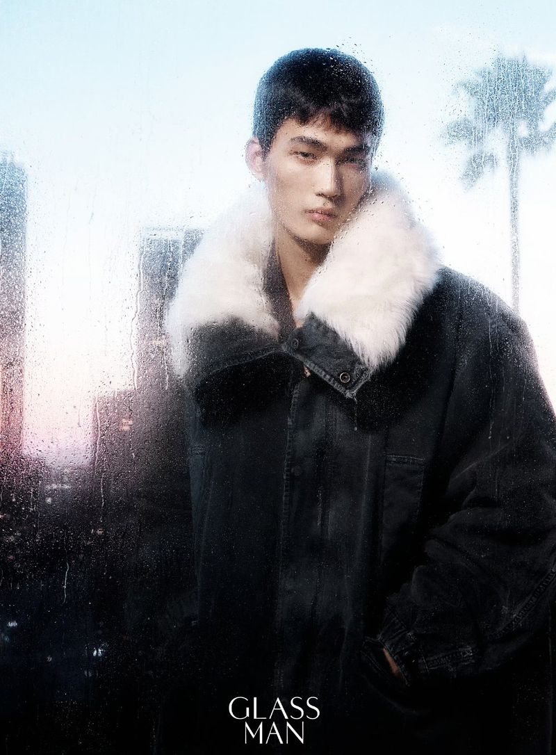 Model wearing a dark coat with a white fur collar posed against a rainy glass window with city silhouettes.