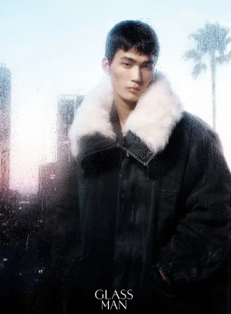 Model wearing a dark coat with a white fur collar posed against a rainy glass window with city silhouettes.