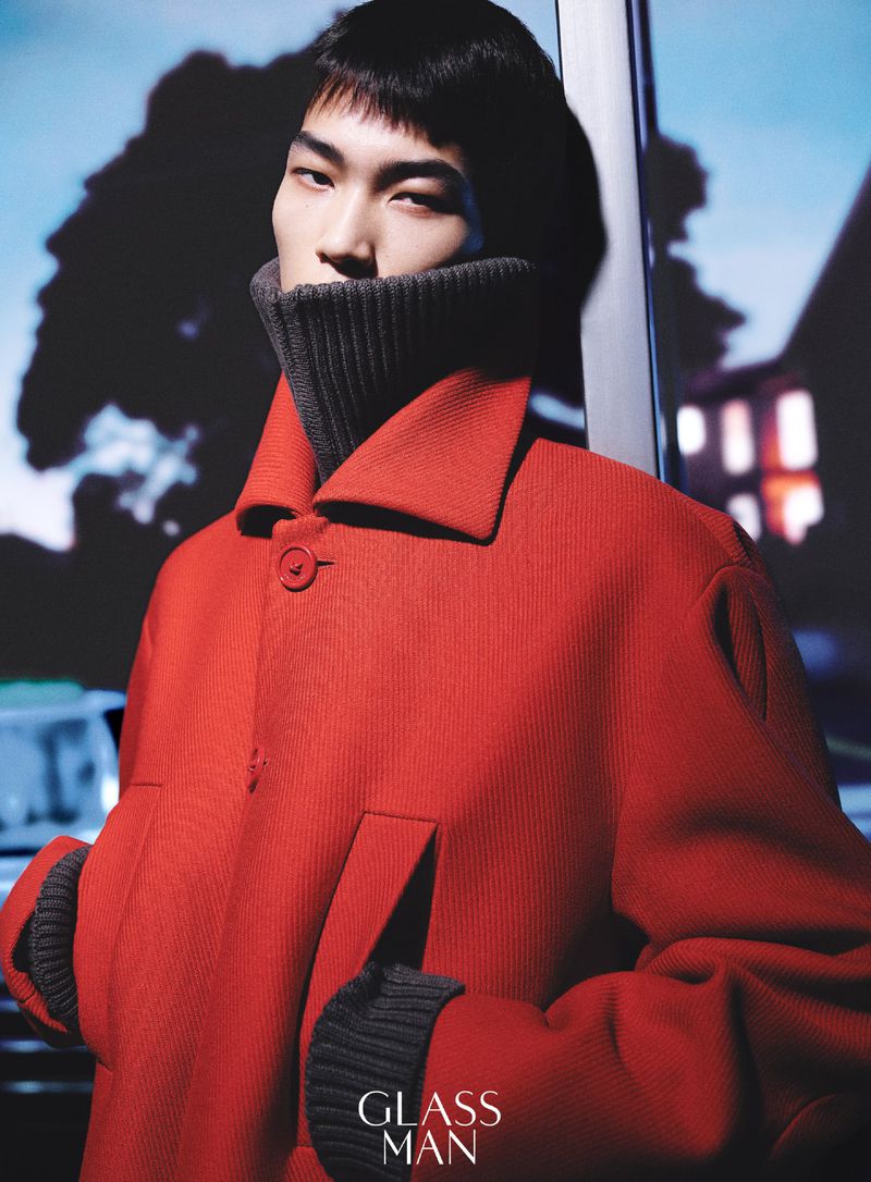 Model wearing a vibrant red coat with a dark turtleneck collar leaning against a wall in a portrait for Glass Man China.