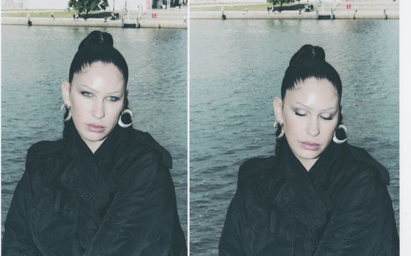Portrait of Eartheater wearing a dark jacket and crescent earrings against a waterfront backdrop, shot by Emil Dietrich.