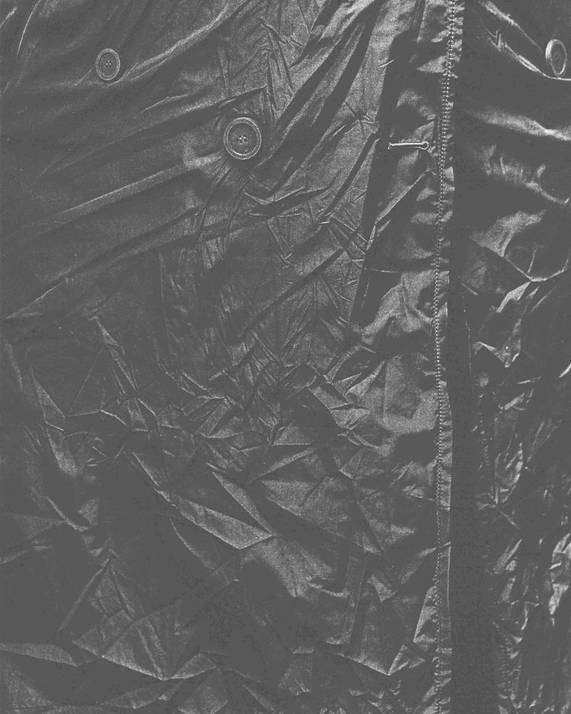 Close-up of heavily creased dark fabric texture with visible buttons and stitching details.