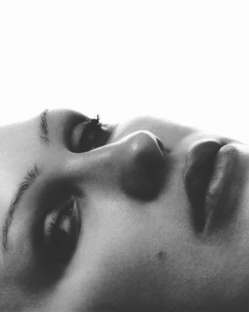 Close-up monochrome portrait of a woman in profile against a bright white background, photographed by Emil Dietrich.