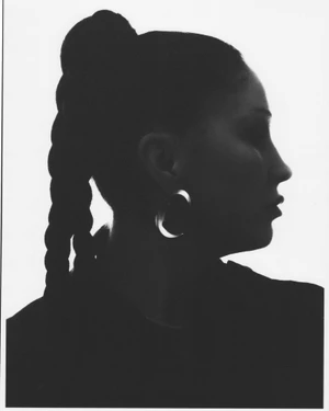 Profile silhouette of a woman with a thick braided ponytail and a large hoop earring against a bright background.