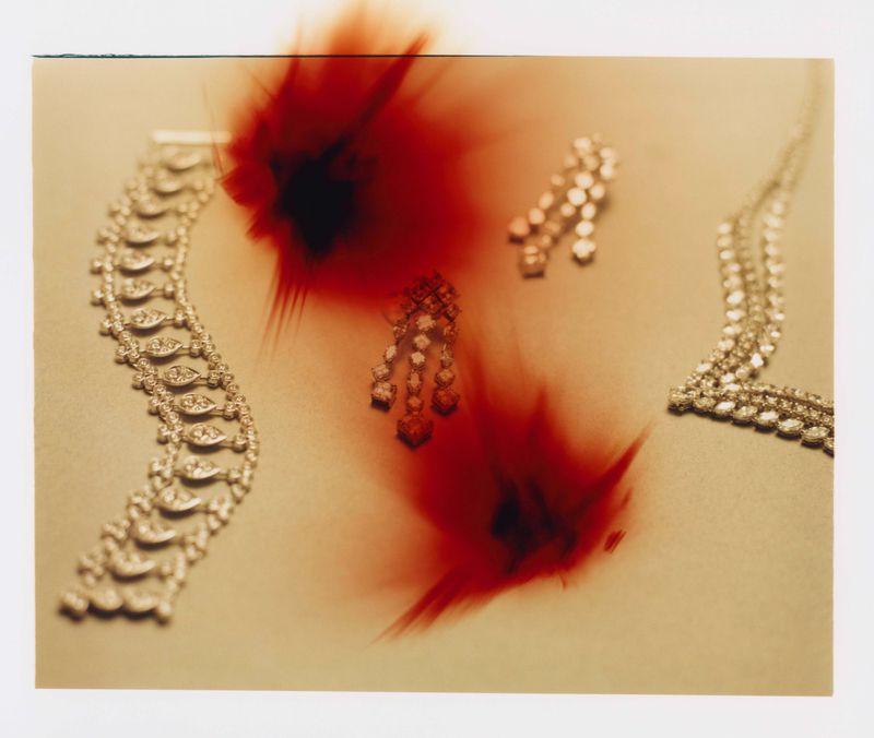 Close-up still life photograph of diamond jewelry on a pale surface with abstract red blurred spots across the frame.