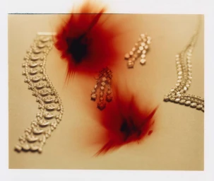 Close-up still life photograph of diamond jewelry on a pale surface with abstract red blurred spots across the frame.
