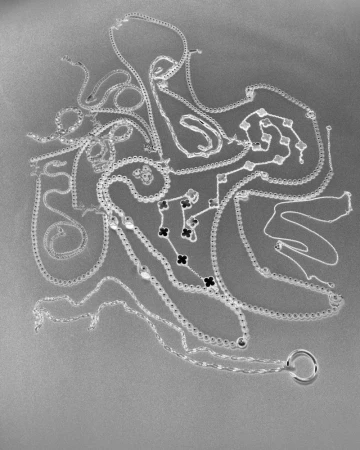 An inverted monochrome flat lay of multiple silver chain necklaces with clover motifs on a grey background