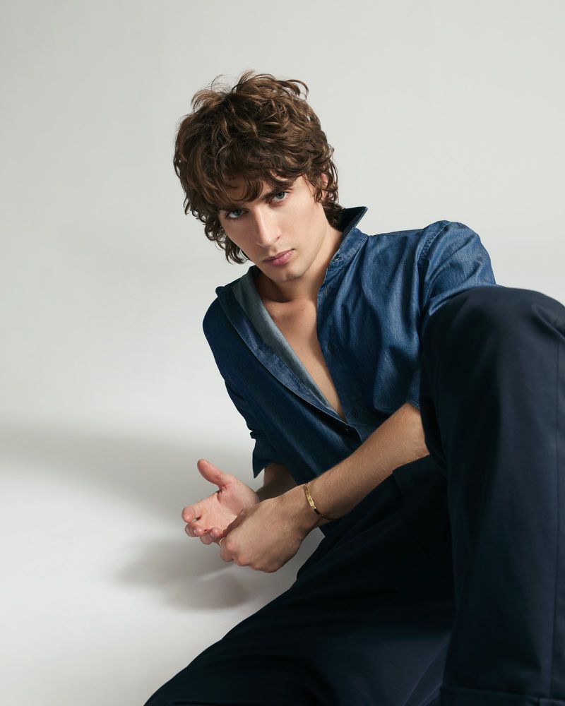 Malcolm McRae wearing a blue shirt and dark trousers against a plain light background for Cosmopolitan Italy editorial
