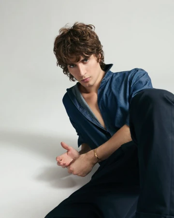 Malcolm McRae wearing a blue shirt and dark trousers against a plain light background for Cosmopolitan Italy editorial