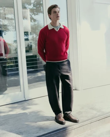 Full-length portrait of a male model wearing a red polo sweater and black trousers standing outside a building