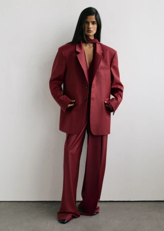 Model standing against a white studio wall wearing a matching burgundy oversized blazer and wide leg trousers