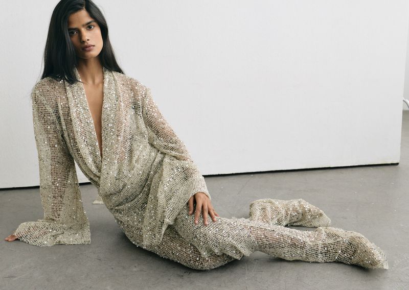 Model seated wearing a sparkling mesh outfit and matching boots against a clean white backdrop