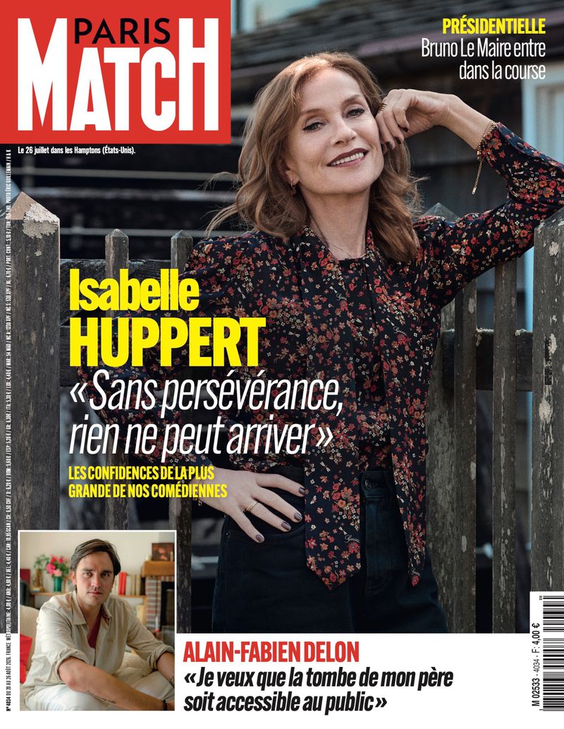 French actress Isabelle Huppert leaning against a wooden fence wearing a floral print blouse and dark trousers for Paris Match July 2026