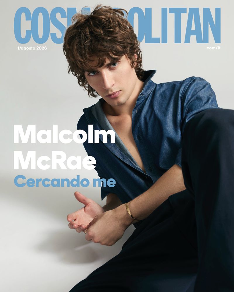 Malcolm McRae wearing a blue denim shirt and dark trousers against a white seamless background for Cosmopolitan Italy.