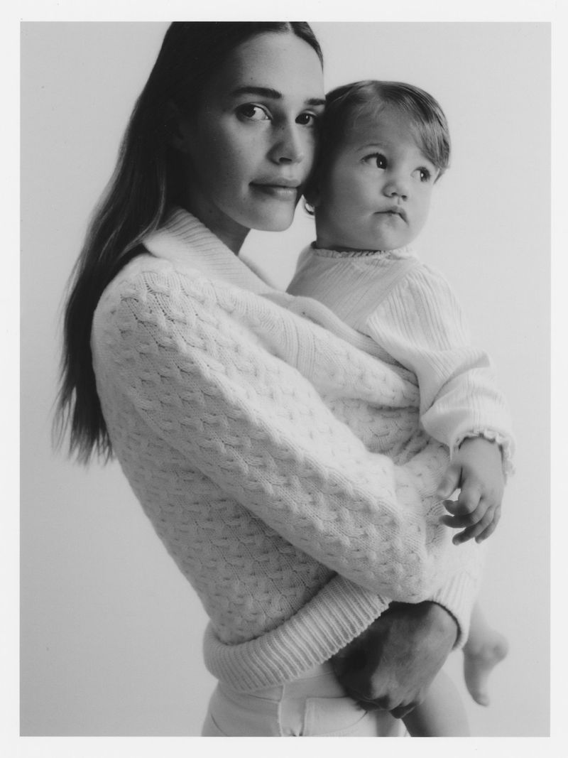 Black-and-white portrait of a woman holding a baby. The woman is wearing a textured sweater, and the baby is wearing a white outfit.