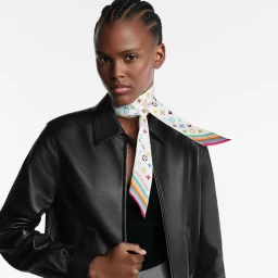 Model wearing a black leather jacket and a colorful monogram silk scarf tied around her neck against a white background