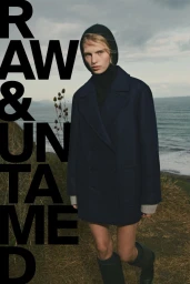 Model in a dark wool coat and hood standing on coastal cliffs above the ocean for Massimo Dutti