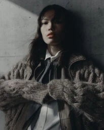 Model in a textured knit sweater and collared shirt posing against a concrete wall for Brunello Cucinelli FW26
