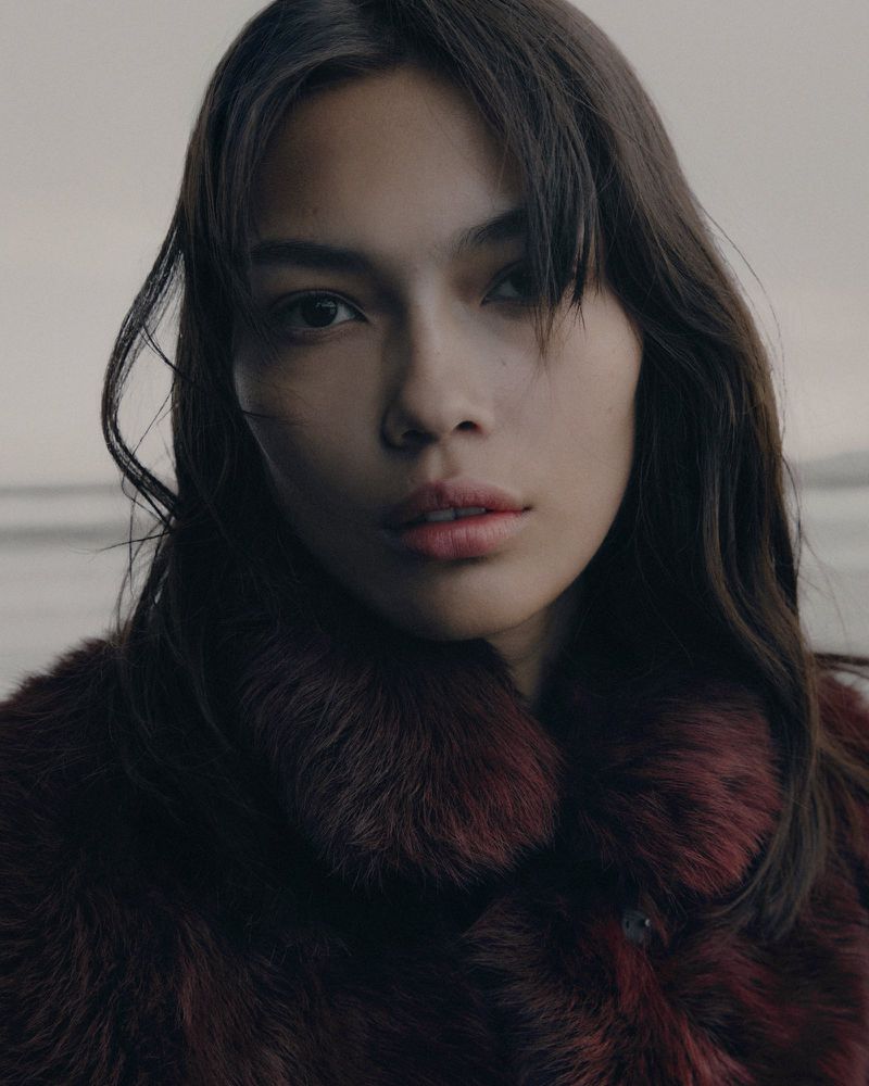 Close-up portrait of a woman wearing a plush textured burgundy winter collar against an overcast background