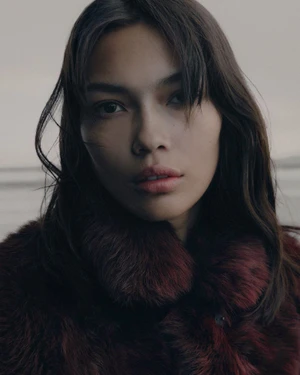 Close-up portrait of a woman wearing a plush textured burgundy winter collar against an overcast background