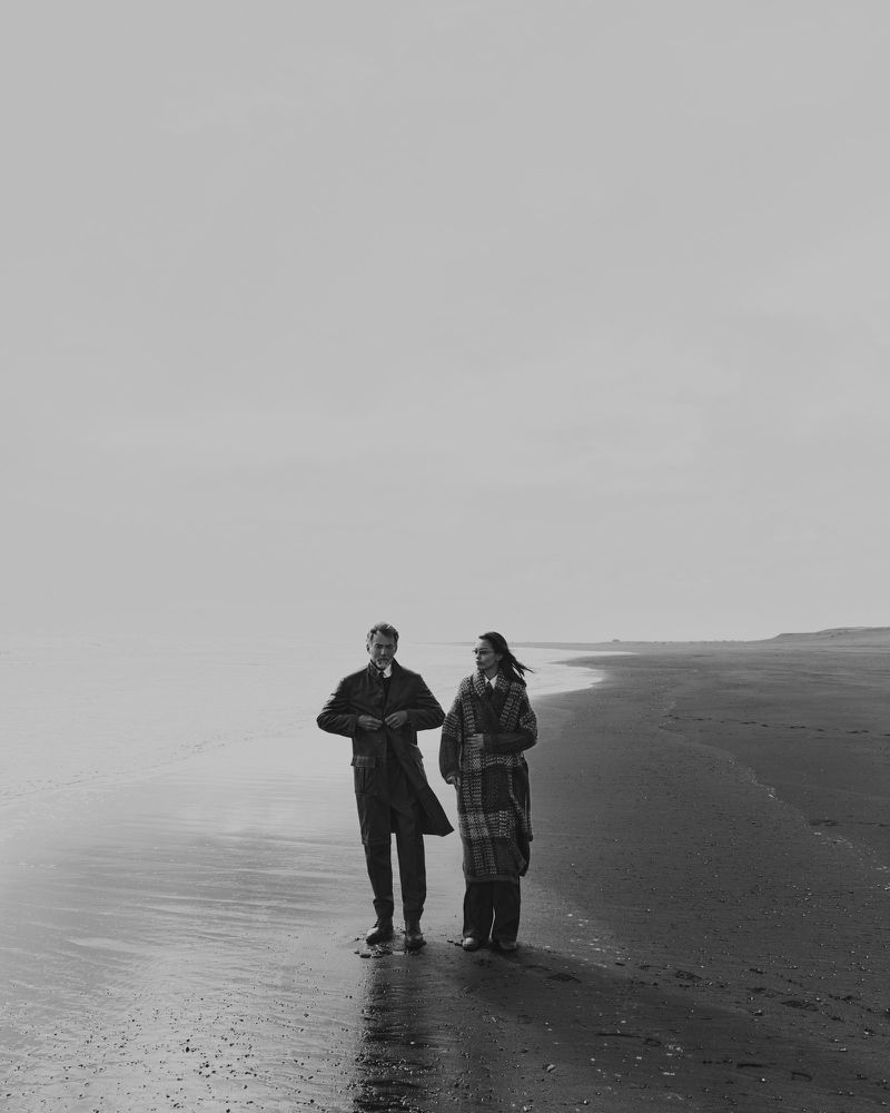Monochrome image of a man and woman walking along a sandy beach under an overcast sky