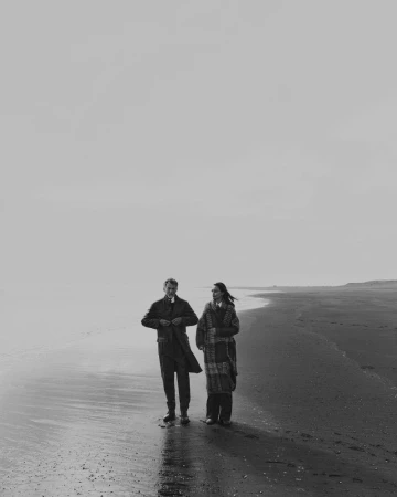 Monochrome image of a man and woman walking along a sandy beach under an overcast sky