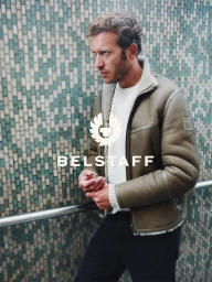 Model in olive shearling jacket and white knit sweater standing against green tiled wall for Belstaff
