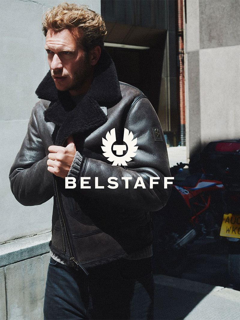 Model wearing a dark leather shearling jacket against a stone building exterior for Belstaff