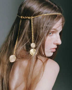 Close-up portrait of a woman with long brown hair wearing a delicate gold chain headpiece with dangling coin charms for Ippolita Campaign