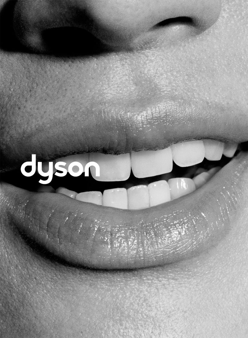 Close-up macro shot of a person smiling with white teeth and visible skin texture, featuring the Dyson logo.