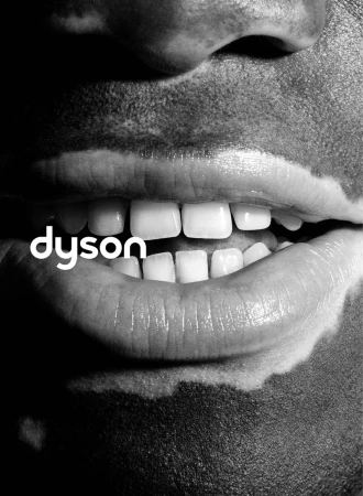 Close-up monochrome portrait focusing on lips and teeth with visible skin pigmentation variations, featuring Dyson branding.