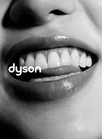 Monochrome close-up portrait focusing on smiling lips and teeth with the Dyson logo visible.
