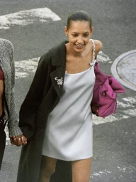 Model in a silver slip dress wearing a dark coat and holding a bright pink handbag on a city street.