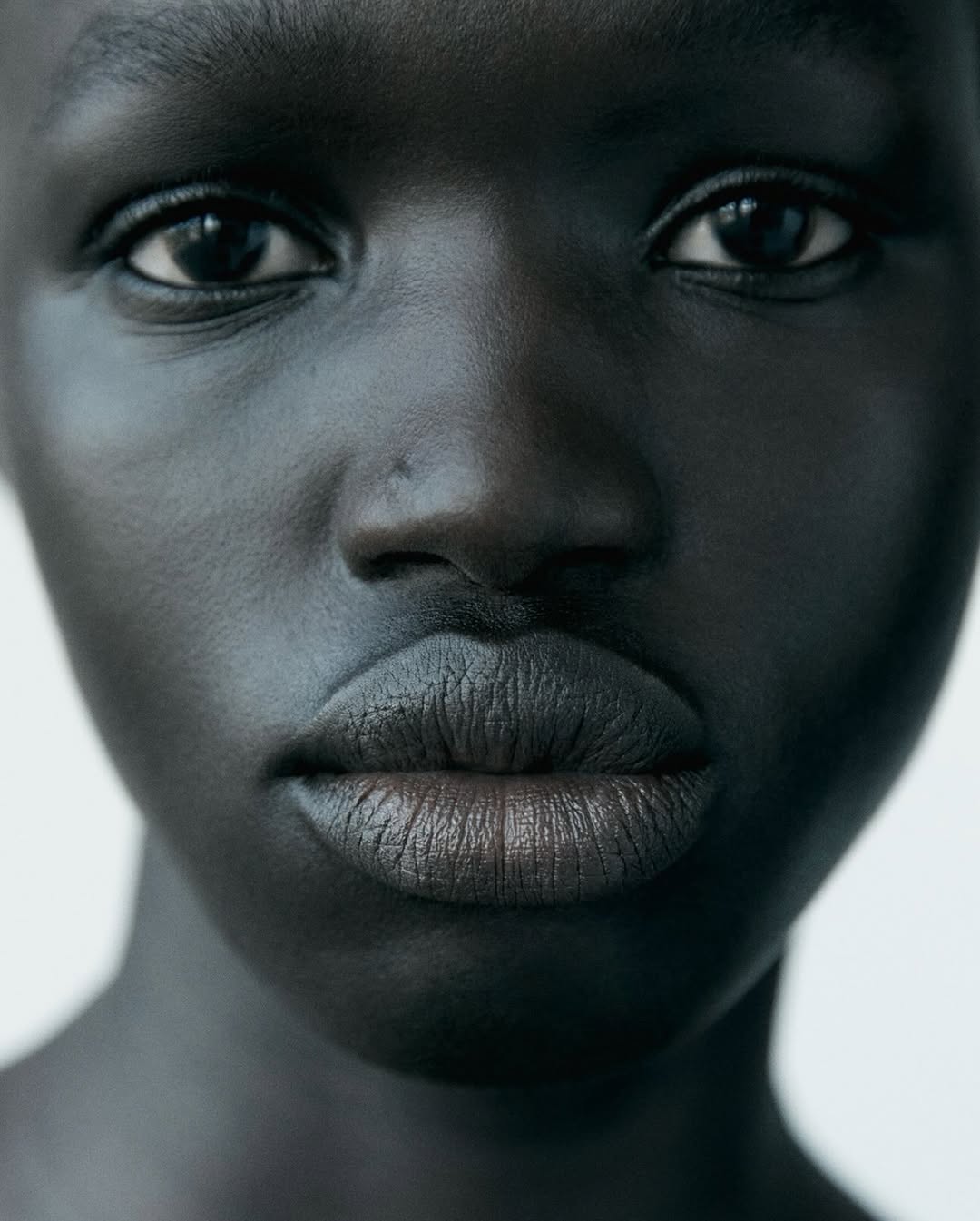 Close-up portrait of an adult African female with dark skin, black eyes, and full lips against a plain white background in a beauty shot.