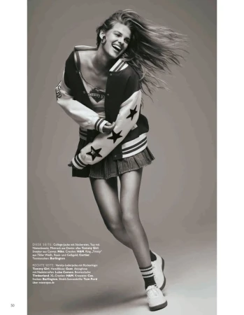 A young woman in a bomber jacket and skirt laughs, her hair flying, posing in a studio. Fashion editorial, black and white.