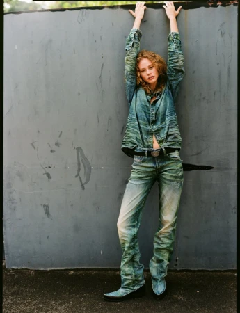 Model Tess Carter posing against a weathered grey wall in a denim outfit for Vogue Netherlands, photographed by Jorin Koers.