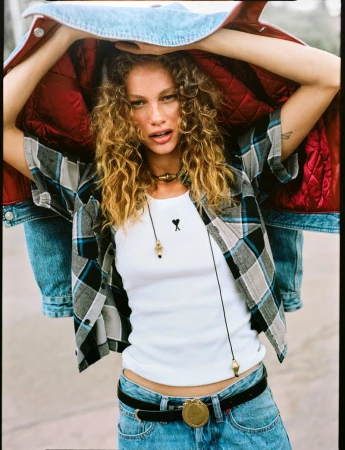 Model with curly blonde hair wearing a plaid shirt and holding a denim jacket overhead for Vogue Netherlands