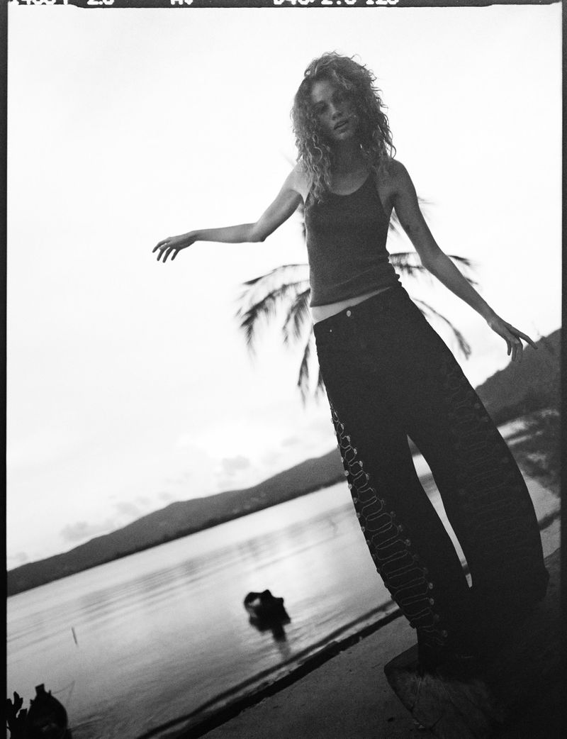 Model with curly hair wearing dark tank top and baggy pants outdoors near water by Vogue Netherlands
