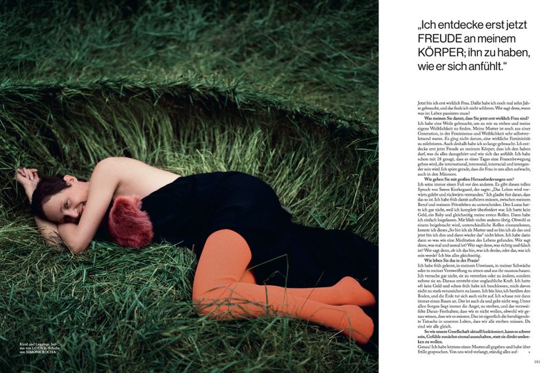 Vicky Krieps lying in tall grass wearing a dark dress and bright orange tights for Vogue Germany