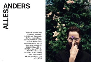 Vicky Krieps holding a purple flower over her eye in front of a rose bush for Vogue Germany ALLES ANDERS editorial