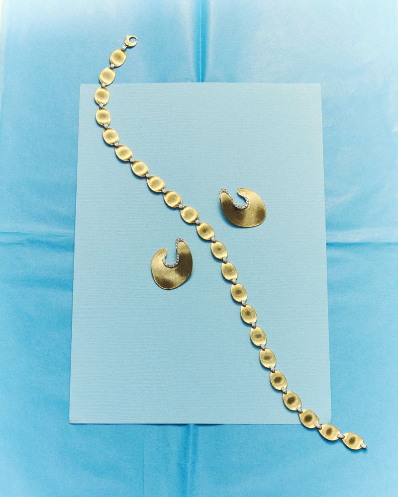 Gold chain bracelet and matching earrings arranged on a light blue paper backdrop for D Repubblica